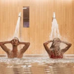 Un couple qui se douche dans une piscine avec deux douchettes à haute pression sur le mur