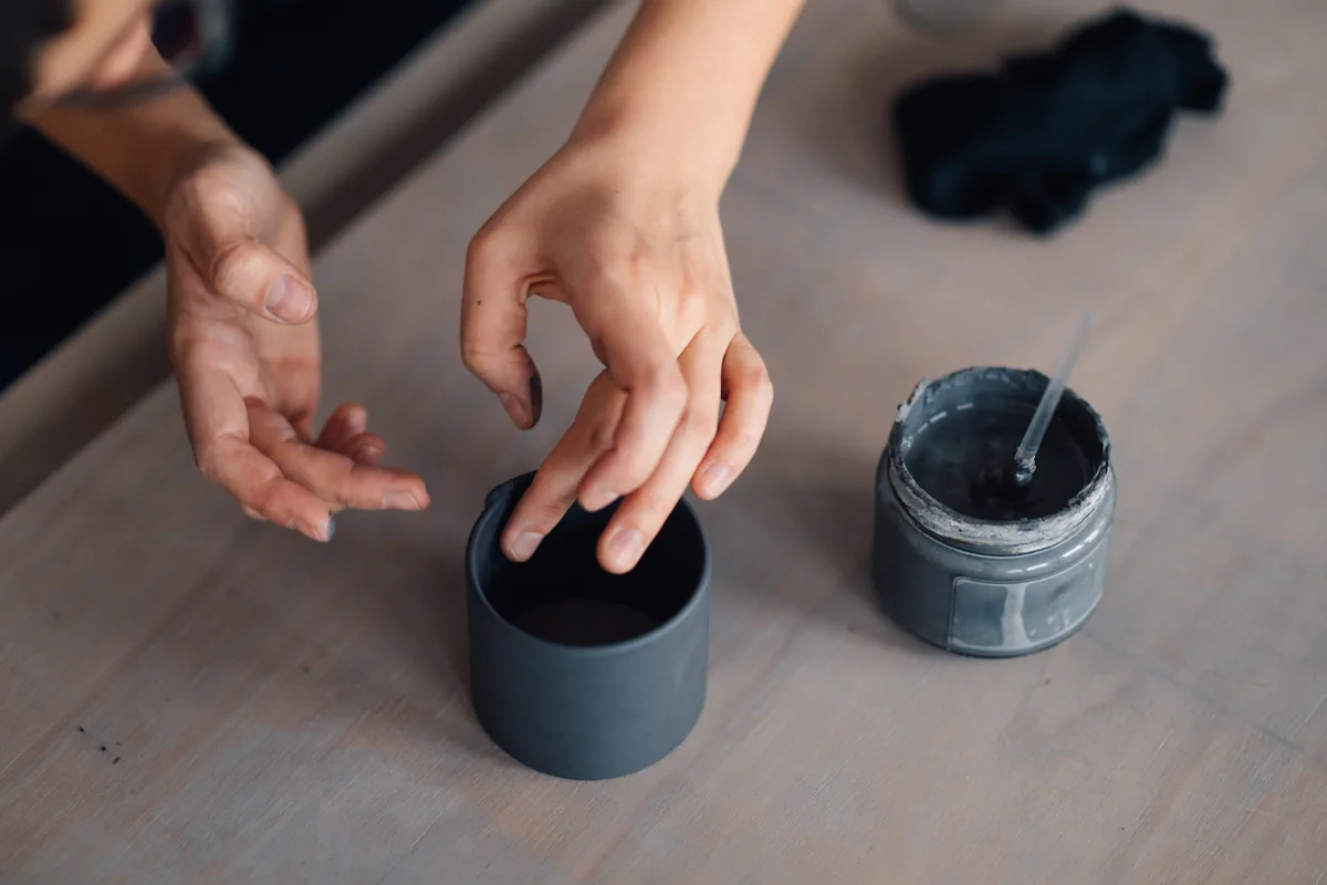 Une personne qui travaille une pâte autodurcissante gris foncé avec un pot de peinture à côté