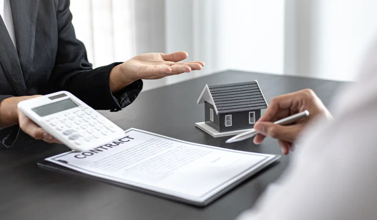 Une personne qui montre une calculatrice à une autre personne surle point de signer un contrat près d'une maquette de maison