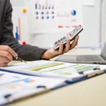 Une personne sur sa calculatrice en regardant des documents
