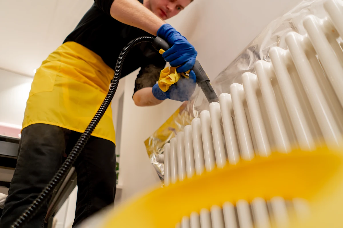 Un homme qui nettoie un radiateur avec un appareil avec un embout noir