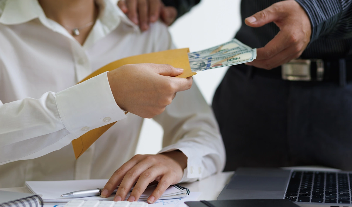 Une personne qui tend de l'argent dans une enveloppe à une autre