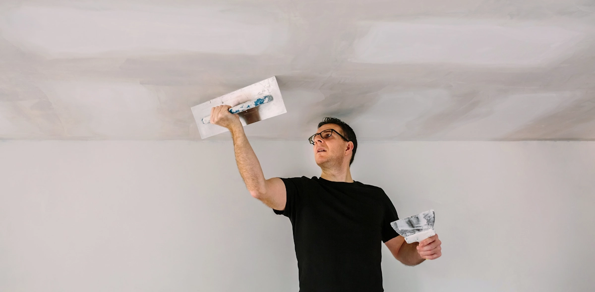Un homme qui rebouche des trous sur un plafond avant la peinture