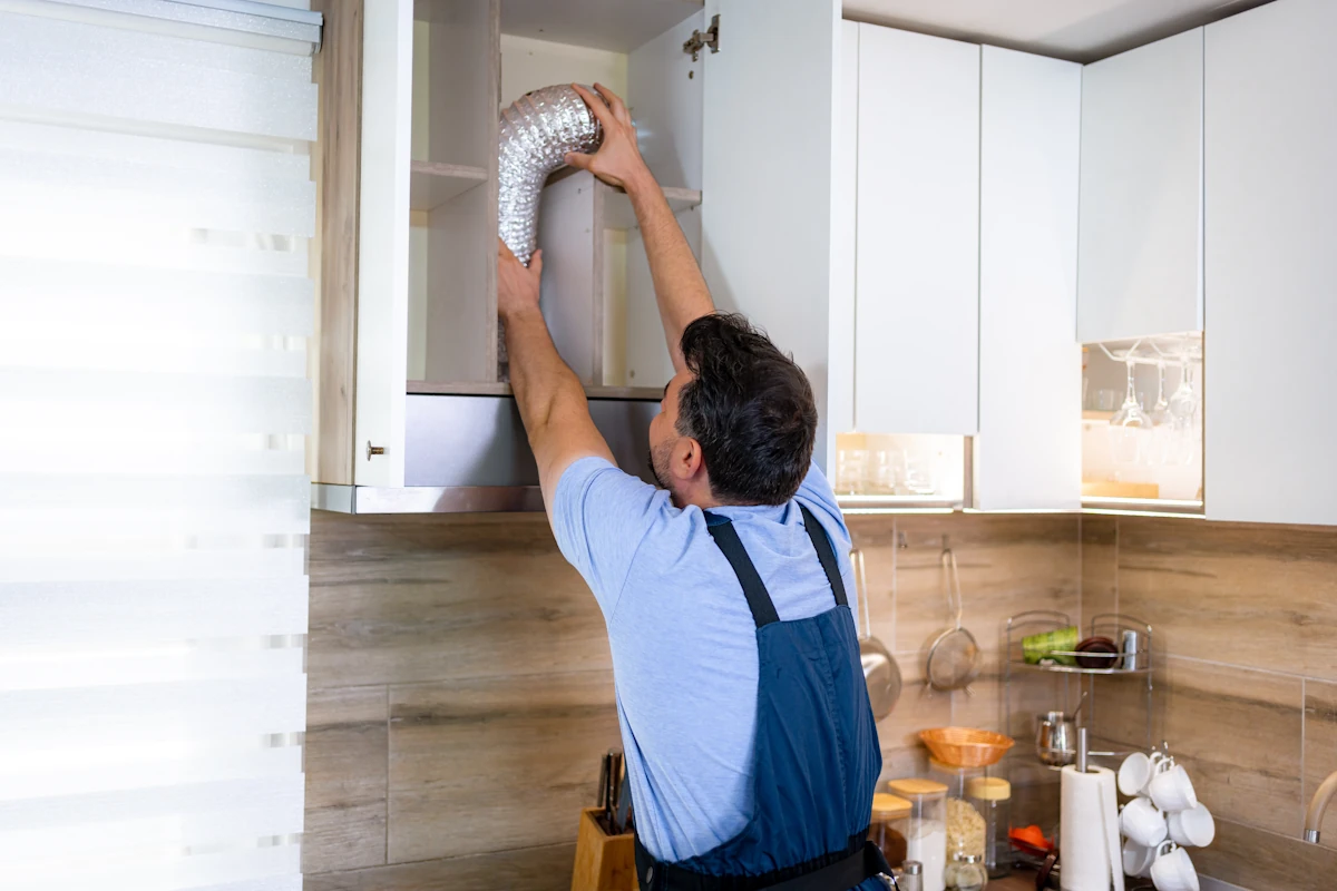 Un homme qui installe un VMC simple flux dans une cuisine